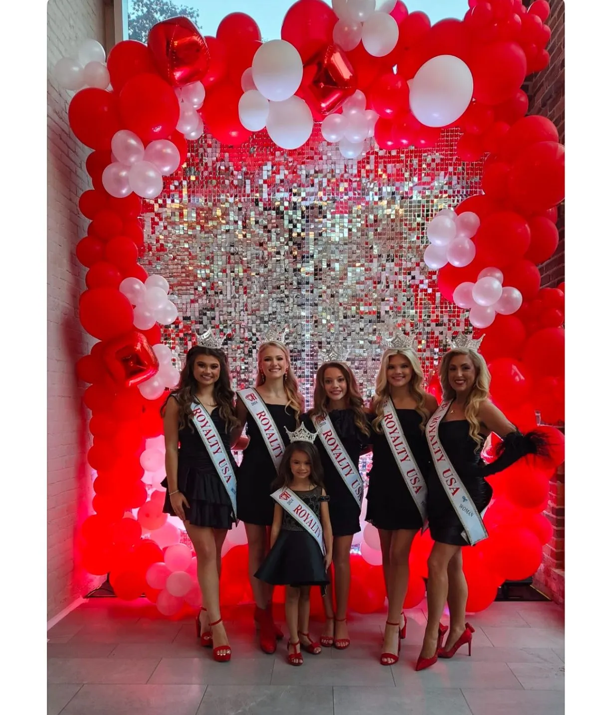 Group of titleholders posing on a red balloon arch with a silver sequin backdrop